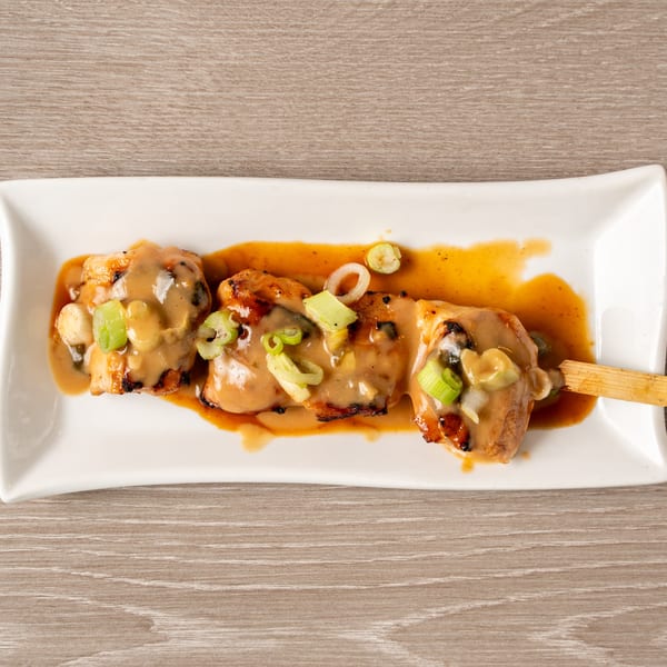 Yakitori chicken skewer with creamy sauce and green onions on a white rectangular plate.