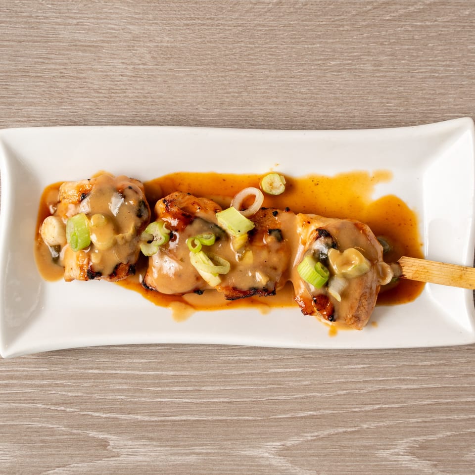Yakitori chicken skewer with creamy sauce and green onions on a white rectangular plate.