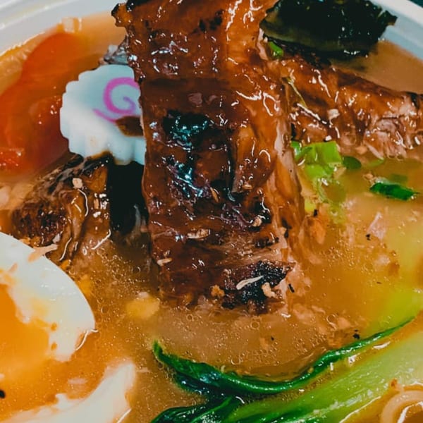 Close-up of Japanese ramen with glazed pork, narutomaki, bok choy, and a soft-boiled egg.
