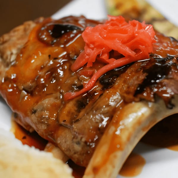 Close-up of a glazed fish head topped with bright red pickled ginger, a Japanese delicacy.
