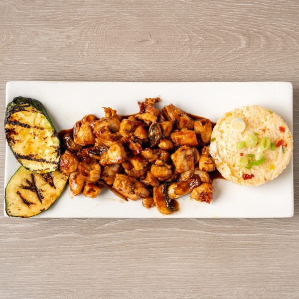 Teriyaki chicken with grilled zucchini and a side of rice, garnished with green onions.