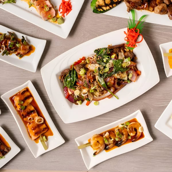 An overhead view of various Japanese dishes, including grilled skewers, beef, and tuna, on a wooden table.
