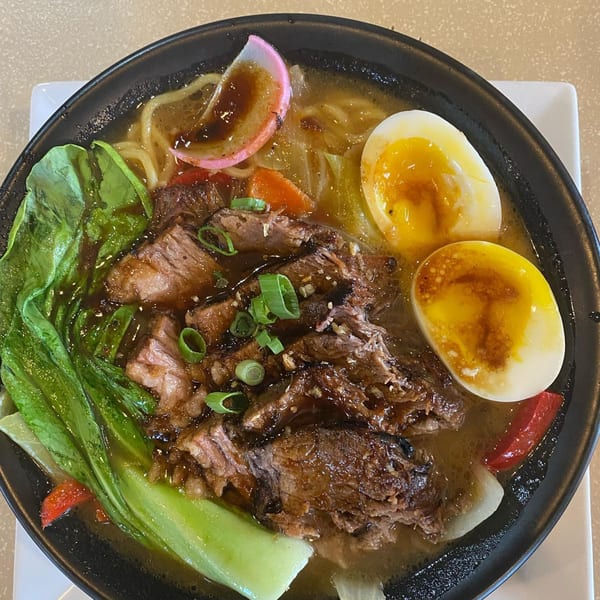 A close-up of Japanese ramen with beef, bok choy, soft-boiled eggs, and fish cake.