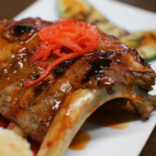 Close-up of a glazed yakitori lamb chop topped with red pickled ginger, served with grilled zucchini.