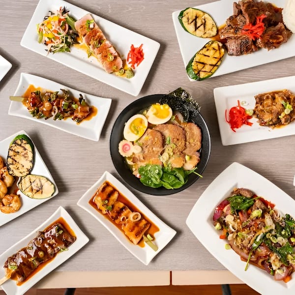 An overhead shot of various Japanese dishes, including ramen, yakitori skewers, and grilled meats.